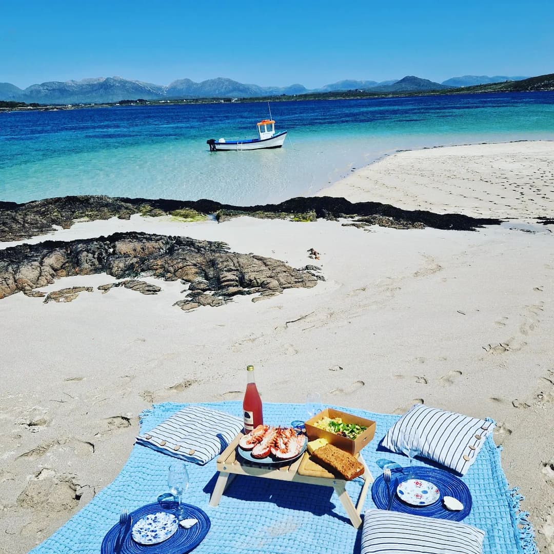 Beach picnic on white sand with a small boat in the turquoise water and the Connemara mountains behind