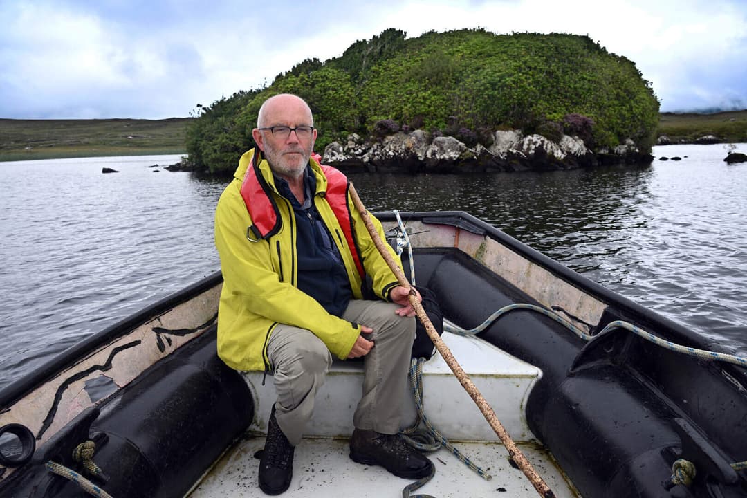 Local guide in a yellow jacket and life jacket sitting in a boat on a Connemara lake